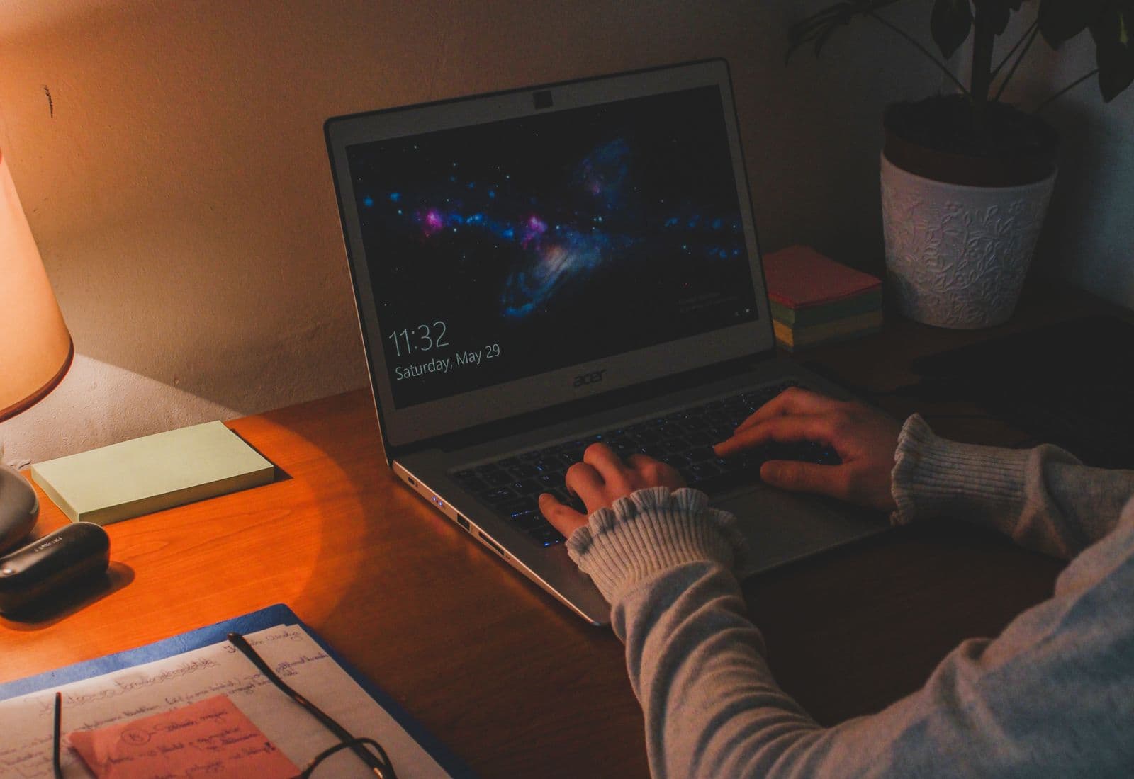 Personne attablée devant un ordinateur portable, les mains sur le clavier, éclairée par une lampe de bureau.